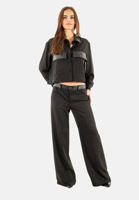 Giacca nera a maniche corte con bottoni e una toppa in pelle a contrasto, abbinata a pantaloni neri a gamba larga. Entrambi realizzati in tessuto liscio; design elegante.