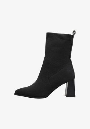 Bottine noire mi-mollet avec bout pointu, talon bloc, bord-côte et languette à l'arrière, présentée sur un fond blanc.