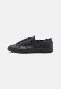 Black sneaker made of textured leather with a low-top design. Features round toe, lace-up front, and rubber sole with a patterned texture.