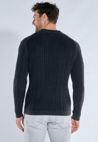 Dunkelgrauer, gerippter Pullover mit langen Ärmeln, rundem Ausschnitt und dezentem Muster. Verfügt über ein Etikett im Nackenbereich.