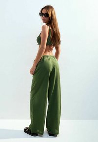 Groene textuur crop top gecombineerd met wijde broek, beide gemaakt van zachte stof. De outfit bevat ook zwarte sandalen en een zonnebril.