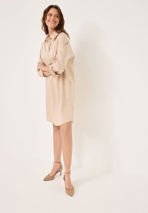 Abito camicia beige con colletto e maniche arrotolate, caratterizzato da una vestibilità rilassata. Abbinato a scarpe con tacco beige con dettagli rossi.