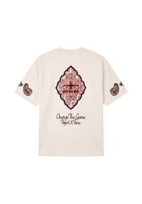 Camiseta crema con diseños de cachemira granate en las mangas y un gran patrón central con el texto "Change The Game Project X Paris" en la parte posterior.