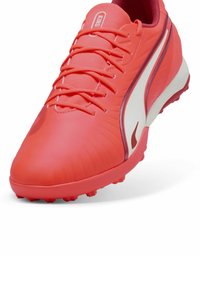 Crampons de football corail vif avec dessus texturé, accents blancs et crampons en caoutchouc vibrants. Comprend sept trous pour les lacets uniformément espacés.