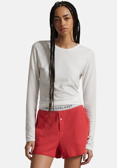 Vit långärmad skjorta tillsammans med röda, ribbade shorts med knapp och midjeband med "POLO RALPH LAUREN"-logotyp.