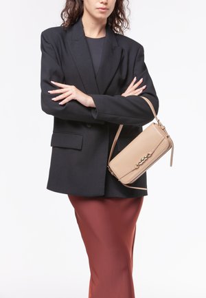 Borsa a tracolla beige con finitura in pelle liscia, forma rettangolare e hardware decorativo. Indossata con un blazer oversize nero e una gonna ruggine.