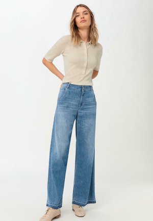 Polo shirt a coste beige chiaro con colletto e bottoni, abbinato a jeans di denim azzurro chiaro a gamba larga con orlo sfrangiato e tasche.