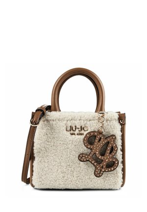 Petit sac à main avec corps en shearling blanc, anses et bordures en cuir marron, et un charm décoratif marron clouté suspendu à l'avant.