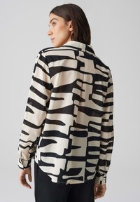 Camicia a maniche lunghe realizzata in tessuto leggero, caratterizzata da un motivo astratto in bianco e nero, con colletto a punta e polsini con bottoni.