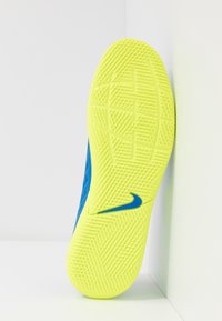 Suela de zapato Nike con patrones texturizados en vibrante amarillo y acentos azules. El diseño es curvado y presenta un destacado logo de Nike.