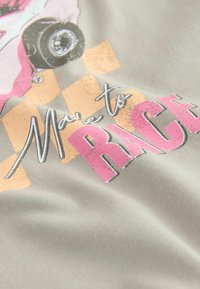 Harmaa kangas, jossa on vaaleanpunaisella ja valkoisella "Made to Race" -painatus, sisältäen kuvan autosta ja ruudullisen taustakuosis.