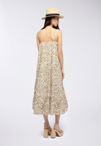 Abito maxi di colore marrone chiaro, con motivo, spalline sottili, forma svasata e bordo arricciato. Abbinato a sandali platform beige e un cappello di paglia.