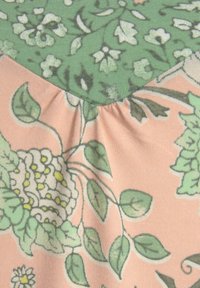 Floral fabric featuring a green top half with white and light green flowers, and a peach bottom half with detailed green leaves and flowers.