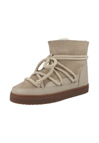 Botín de tobillo beige con base de cuero liso y parte superior de ante, suela de goma gruesa y texturizada, y cordones de cuerda trenzada.