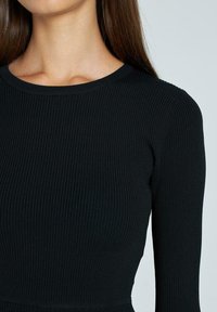 Top nero a coste con maniche lunghe e scollatura tonda. Design aderente con una texture liscia, che mette in mostra uno stile semplice e minimalista.