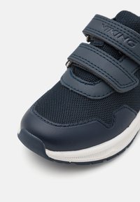 Marineblå sneakers med nettingoverdel, syntetiske detaljer og doble Borrelås-stropper. Tekstursgummi såle med hvite detaljer.