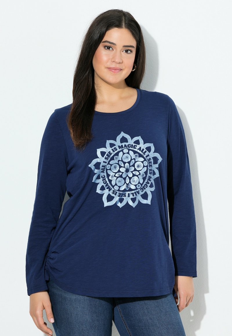 Haut à manches longues bleu marine avec un col rond. Présente un graphique de mandala circulaire en bleu clair avec du texte. Tissu doux et texturé avec un détail de fronces sur les côtés.