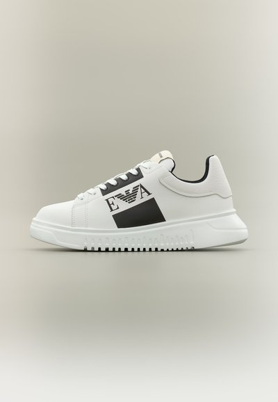 Άσπρο αθλητικό παπούτσι χαμηλού ύψους με μαύρο λογότυπο EA και γραφικά στο πλάι, άσπρη σόλα με υφή για κράτημα και μαύρη εσωτερική επένδυση.