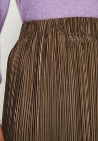 Bruine geplooide rok met een elastische tailleband, gemaakt van een glad materiaal. De stof vertoont verticale, uniforme plooien die de textuur benadrukken.