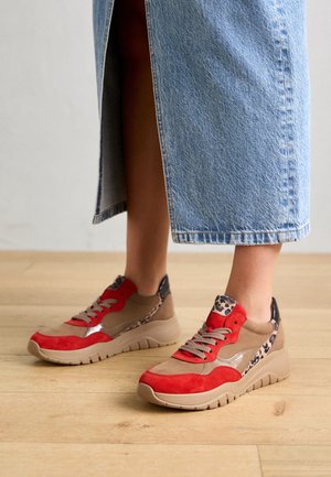 Persoon draagt een mid-lange spijkerrok en beige sneakers met rode accenten en luipaardprintdetails op een houten vloer.
