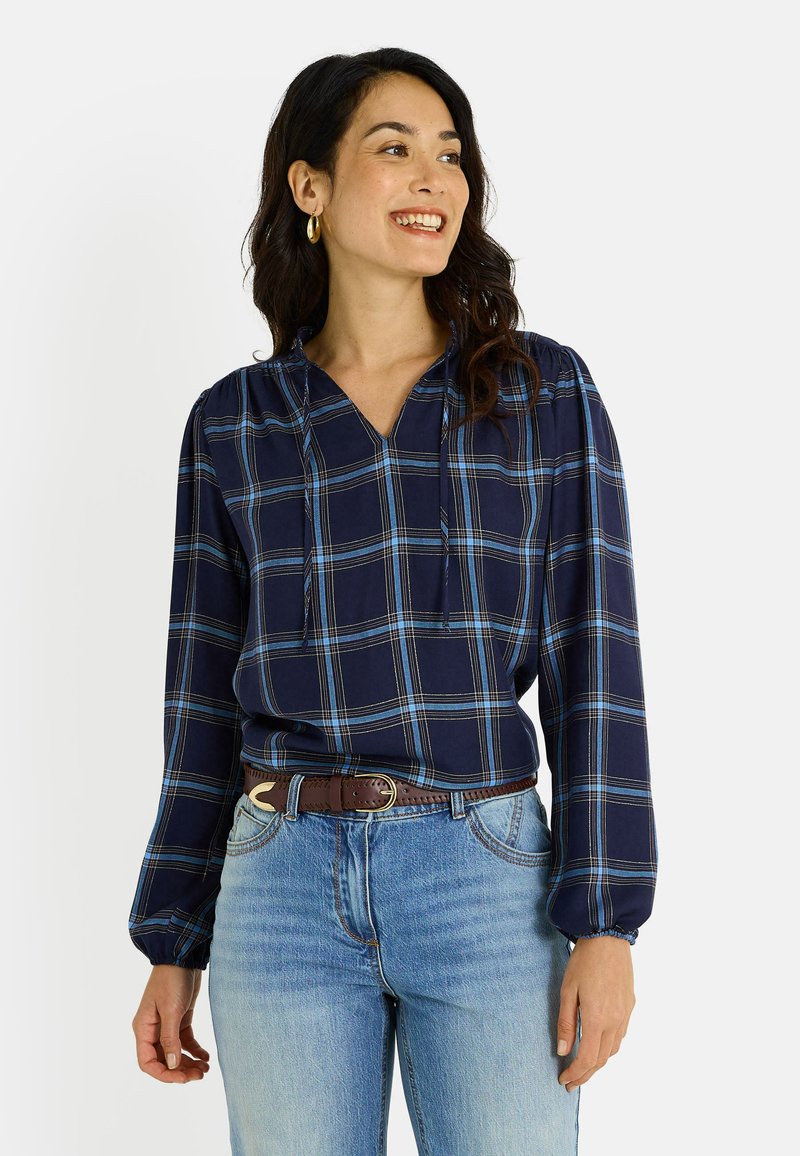 Blouse à manches longues à carreaux navy avec un col en V et un détail à cordon. Tissu doux et léger. Associé à un jean léger taille haute bleu clair.