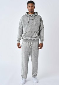 Grijze geborstelde fleecetop met een voorzak en trekkoorden, gecombineerd met bijpassende sweatpants en witte sneakers, met zichtbare stiksels.