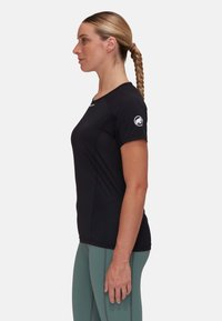 Svart sporttröja med korta ärmar och rund halsringning. Har en logotyp på vänster ärm. Matchas med ljusgröna leggings.