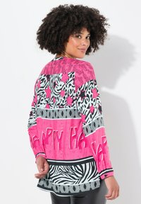 Langsleeve shirt met een mix van gedurfde roze, zwarte en witte patronen, waaronder panterprint en sterren, met de tekst "HAPPY."