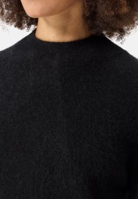 Svart stickad tröja med rund hals, gjord av mjukt, strukturerat material. Tyget ser luddigt ut och har en enhetlig, mörk finish.