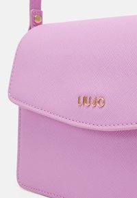 Růžová syntetická kabelka s texturovaným povrchem, klopovým uzávěrem a zlatým logem "LIU-JO". Má prošívání podél okraje.