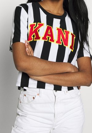 Camiseta corta a rayas en blanco y negro con letras rojas "KANI"; de mangas cortas, hecha de una tela suave con dobladillo recto. Combinada con jeans blancos.