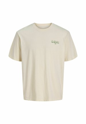 T-shirt écru à manches courtes avec col rond, avec un petit texte vert "La Dependencia la FRANCA" sur le haut gauche de la poitrine.
