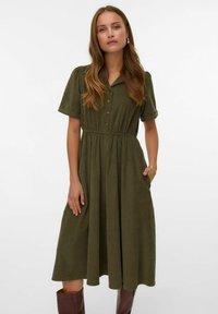 Vestido verde oliva con botonera frontal, mangas cortas enrolladas, cintura ceñida y bolsillos laterales, confeccionado en una suave tela texturizada.