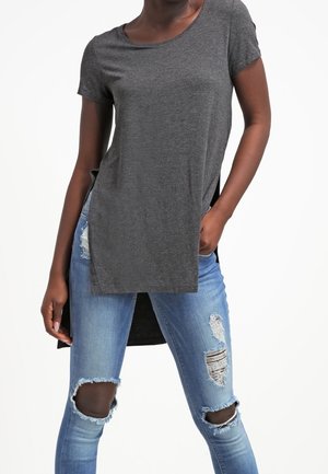 Top grigio a maniche corte con scollatura rotonda e spacchi laterali, abbinato a jeans blu strappati con strappi alle ginocchia e orli sfrangiati.