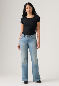 Čierny rebrovaný top s krátkym rukávom, skombinovaný so svetlomodrými rozšírenými džínsami. Džíny majú vyblednutý vzhľad a viditeľné švy. Čierne topánky.