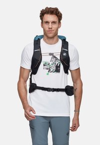 Czarny i niebieski plecak wielokomorowy z regulowanymi paskami, noszony na białej koszulce z grafiką gór i zielonymi akcentami.