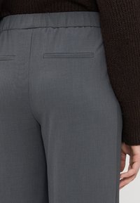 Hellgraue weit geschnittene Hose mit einem elastischen Bund. Verfügt über zwei Taschen auf der Rückseite mit flachen Nähten. Glattes, strukturiertes Gewebe.