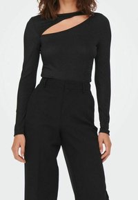 Svart långärmad topp med ett urtag i halslinjen, tillverkad av ett glittrigt material. Följt av högmidjade svarta byxor.