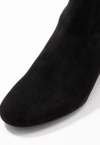 Schwarze Wildleder-Stiefelette mit spitzem Zehenbereich, glatter Oberfläche und minimalem Nähdetail. Die Stiefelette hat einen niedrigen, flachen Absatz.