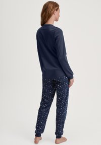 Marineblauwe longsleeve top met een ronde hals, gecombineerd met gestreepte pyjamabroeken versierd met halve maan vormen en subtiele accenten rond de enkels.