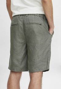 Grønne linshorts med en teksturert overflate, som har to baklommer og en subtil merkeetikett n�ær den høyre lommen.