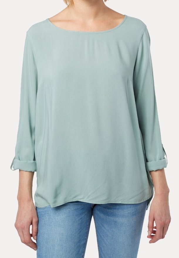 Ljusgrön blus med en slät textur, rund halsringning och trekvartslånga ärmar, som har rullade manschetter och en avslappnad passform.