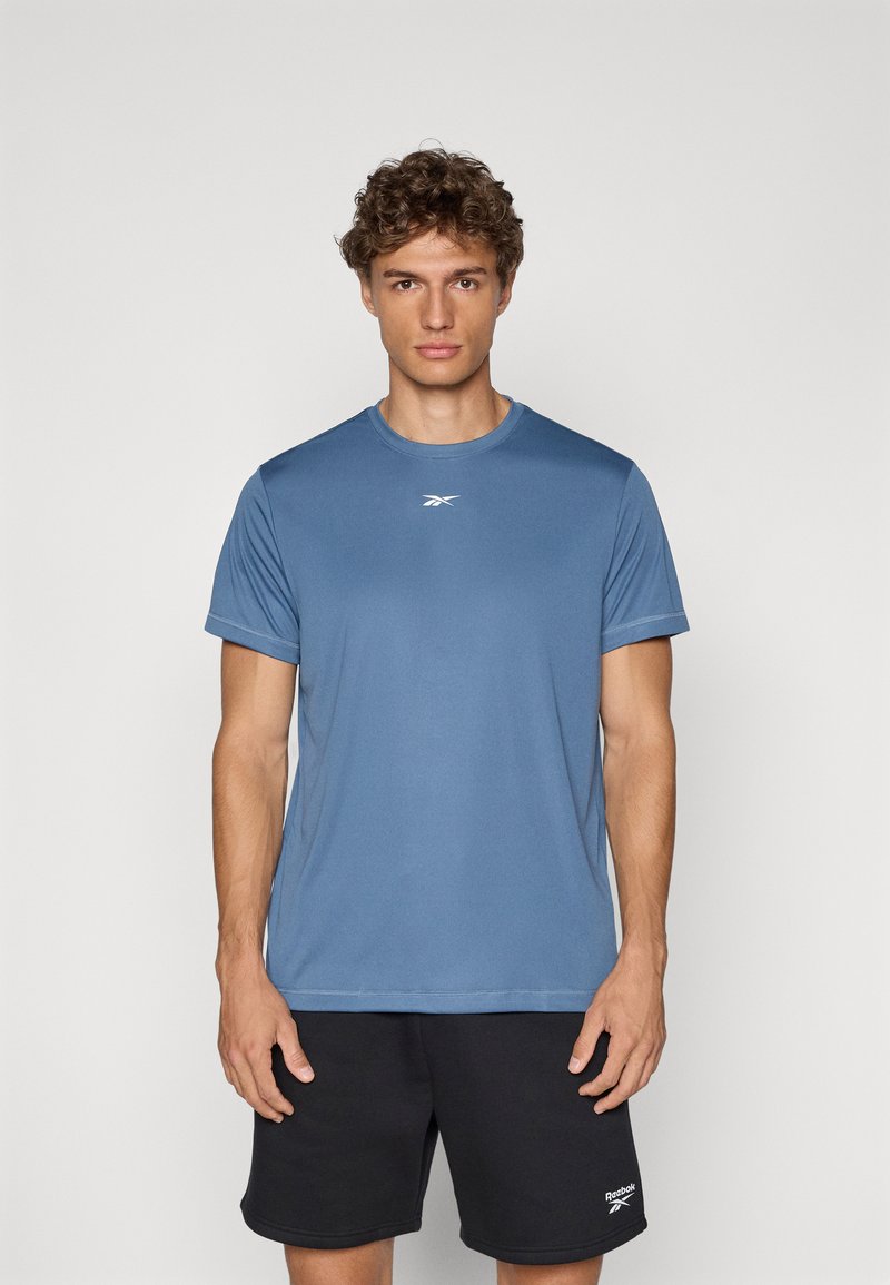 T-shirt de sport bleu en tissu léger, avec un col rond, des manches courtes et un petit logo blanc sur la poitrine.
