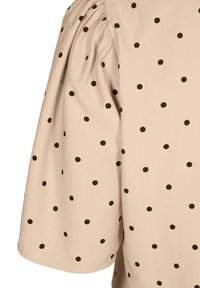 Beige Bluse mit kurzen Ärmeln und braunen Polka-Dots, mit gerafften Schulterdetails und glatter, leichter Textur.