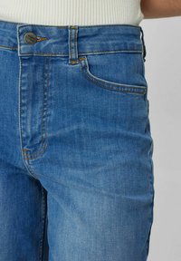 Modro visoko pasovanje iz jeansa iz mehkega denima, z gumbom za zapiranje, petimi žepi in diskretnimi oranžnimi šivi.