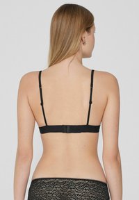 Černá podprsenka s nastavitelnými ramínky, zapínáním na háčky a hladkým textilním povrchem, zobrazená zezadu.