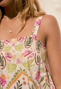 Robe fleurie avec un corsage froncé, de fines bretelles et un tissu léger aux motifs botaniques vibrants en rose, vert et orange.