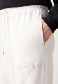 Pantaloni della tuta bianchi con cintura elastica, dotati di un logo del marchio ricamato in bianco sulla coscia e di una tasca laterale.