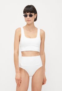 Hvit todelt badedrakt med firkantet hals og høy midje, glatt tekstur og minimalistisk design.