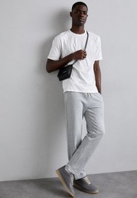Biely bavlnený tričko, šedé tepláky a šedé tenisky so svetlo hnedými podrážkami. Malá čierna crossbody taška na pleci. Jednoduchý, neformálny outfit.